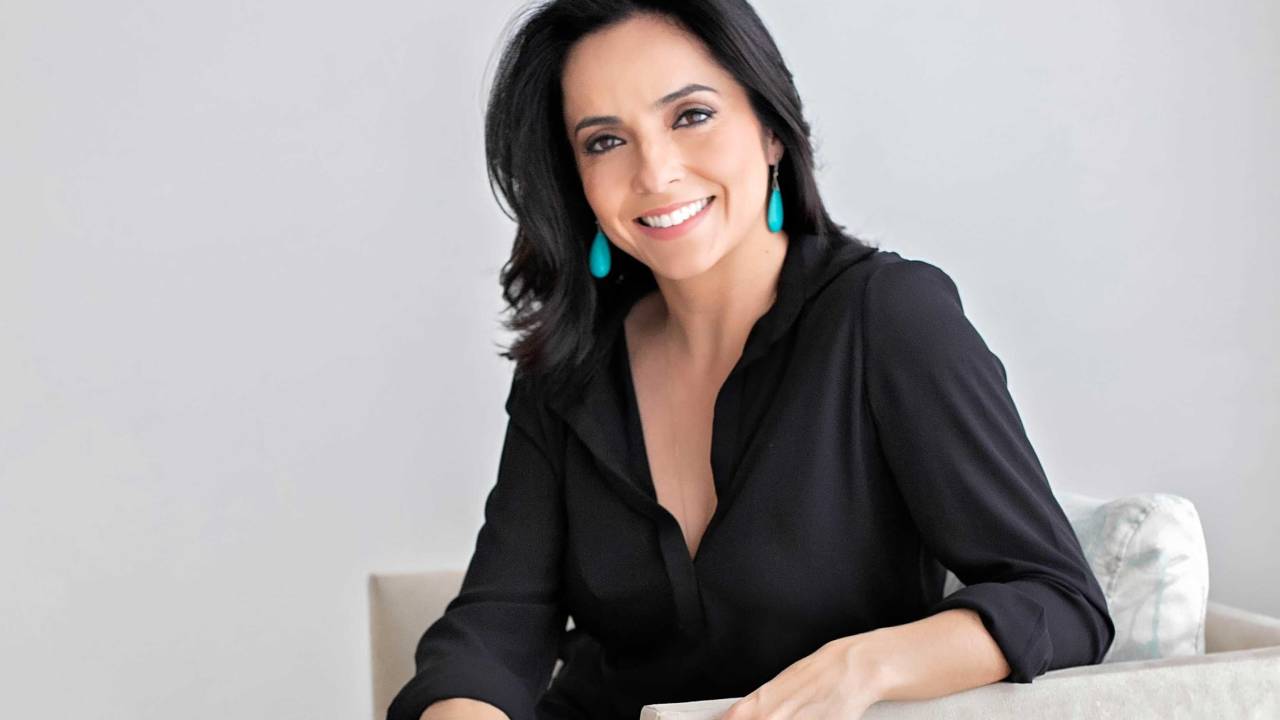 Foto de Izabella Camargo, mulher branca de cabelos pretos sentada numa cadeira e sorrindo