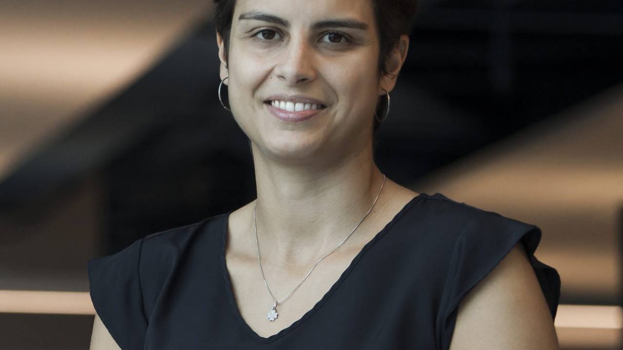 Imagem mostra Flavia Caroni, uma mulher branca, de cabelos escuros e curtos, que está sorrindo para a foto