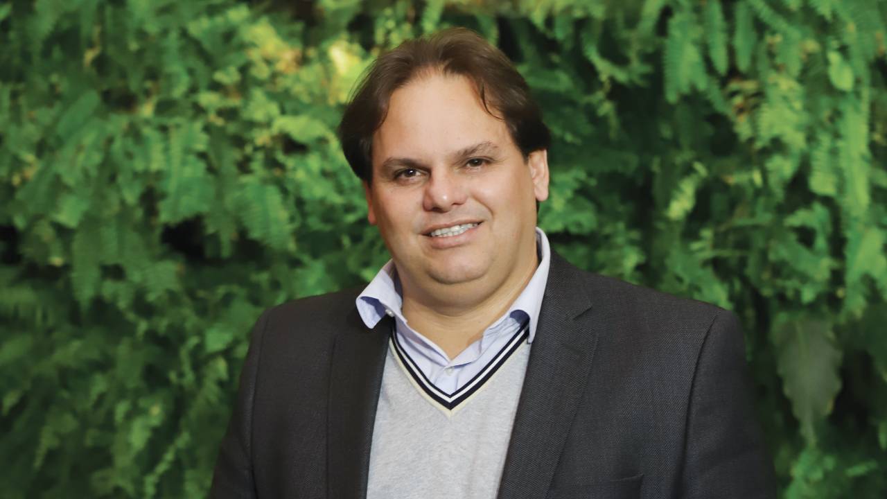 Rodrigo Posa de camisa e blazer preto em frente a uma parede repleta de plantas