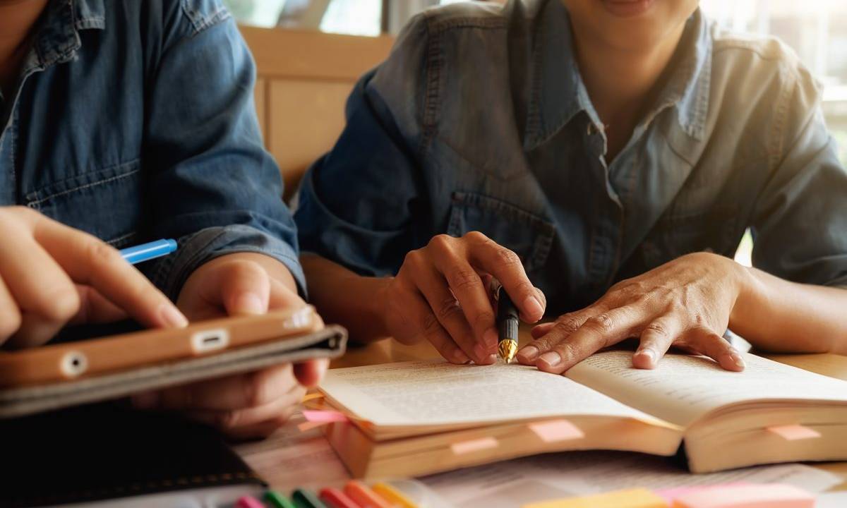 duas pessoas estudando juntas, com livros e canetas na mesa a sua frente