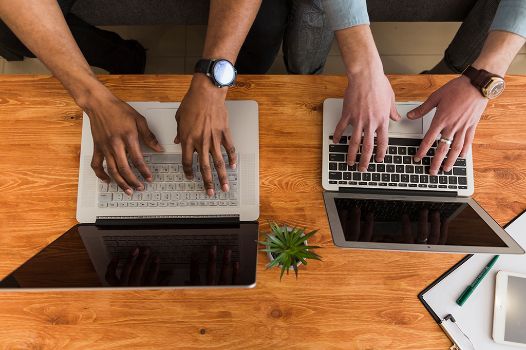 Visão superior de duas pessoas usando laptop em cima de uma mesa de trabalho.