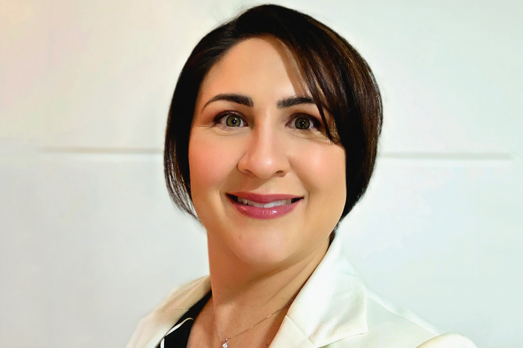 Imagem de uma mulher sorridente, de cabelo curto e escuro, vestindo um terno branco.