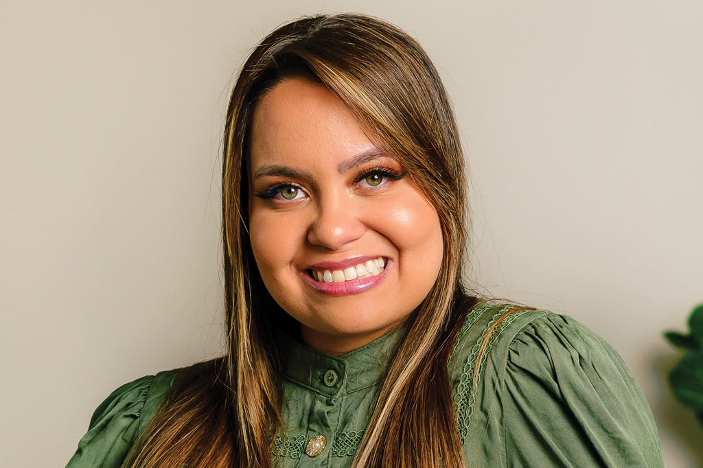 Imagem, em fundo bege, de uma moça sorridente, vestindo uma roupa verde.